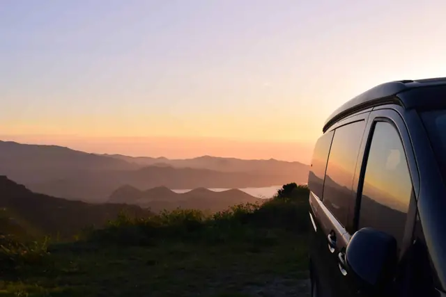 Atardecer sobre las montañas con un monovolumen negro en primer plano